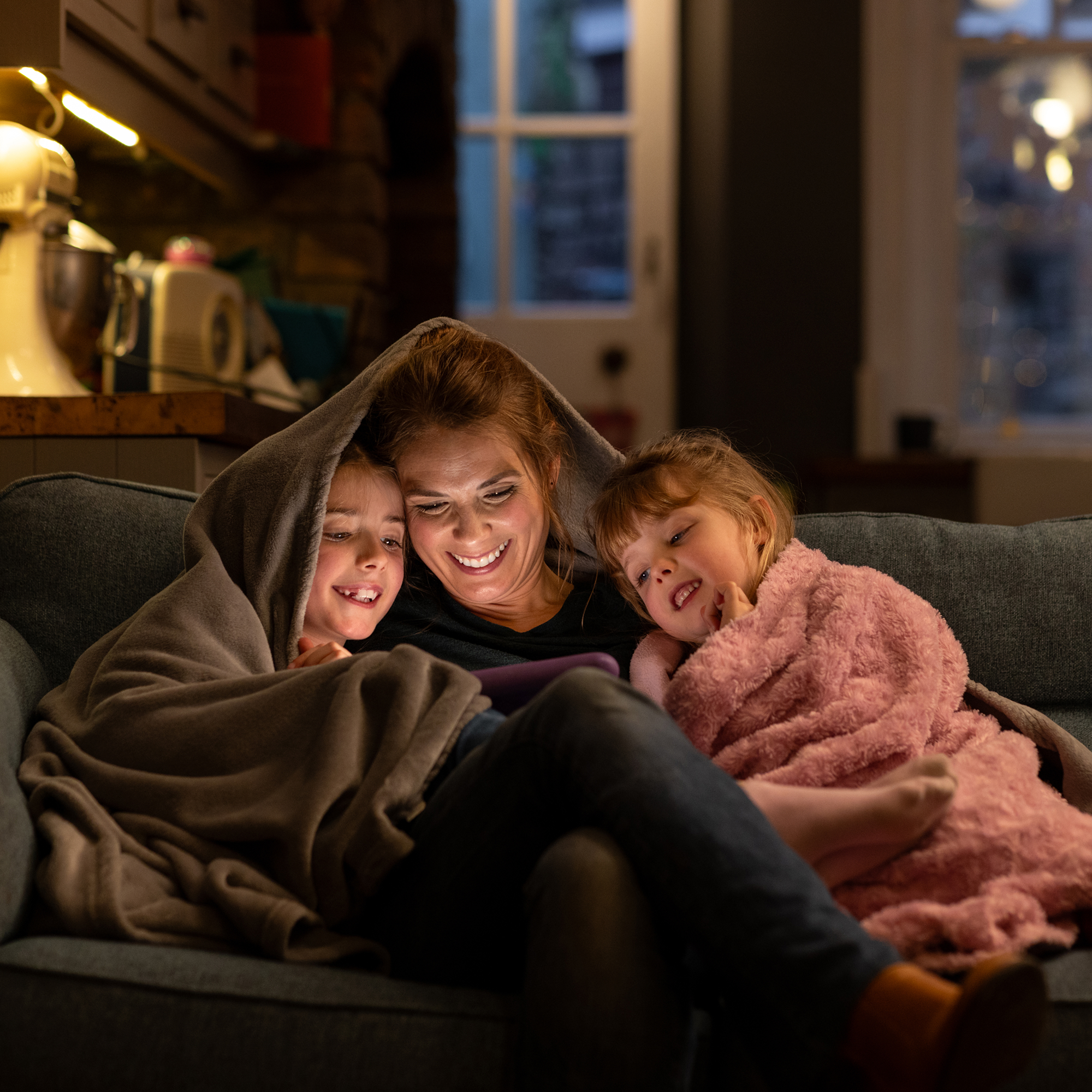 Family looking at tablet under a blanket.