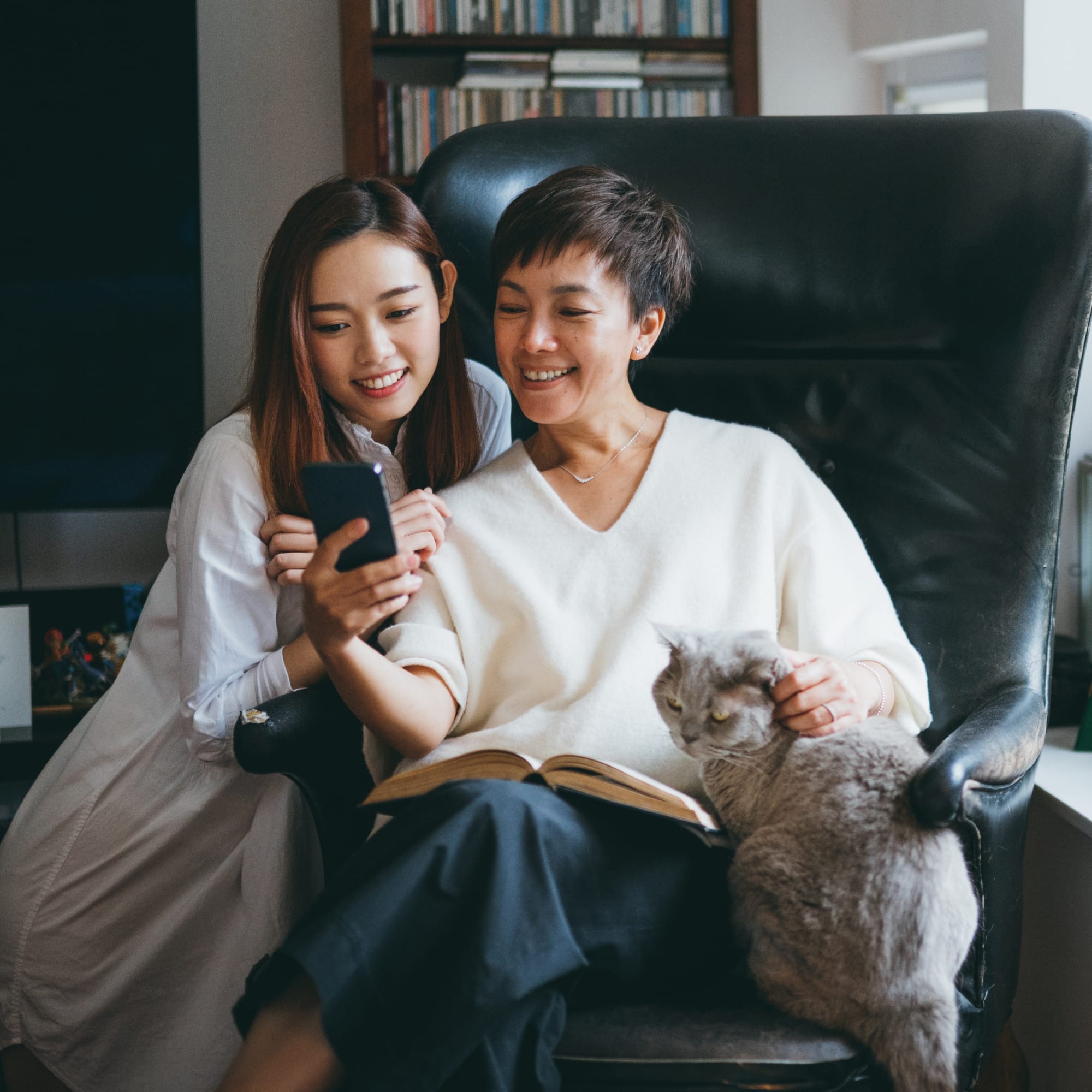 Two woman sitting with a cat and looking at a phone.